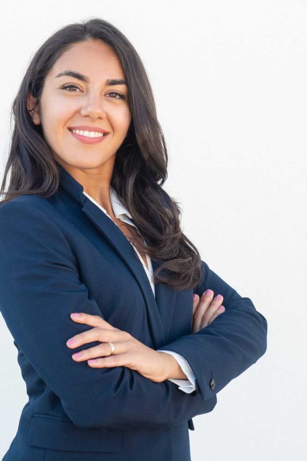 Smiling confident businesswoman posing with arms folded. Happy beautiful black haired young Latin woman in formal suit standing for camera over white studio background. Corporate portrait concept